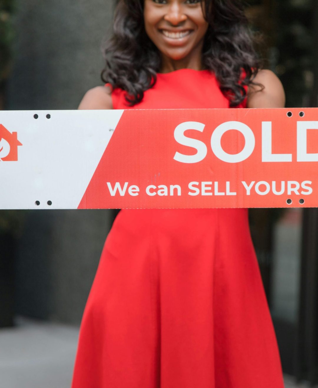 Smiling woman holding a 'Sold' sign, symbolizing successful real estate sales.