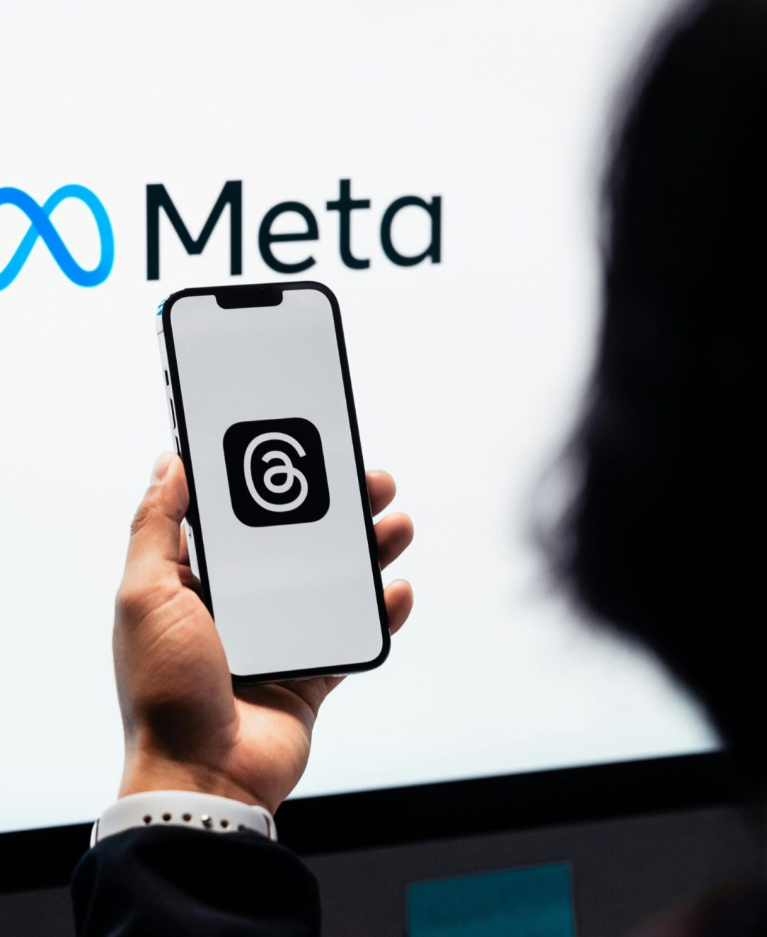 Hands holding smartphone with Meta Threads logo on screen, Meta branding in background.