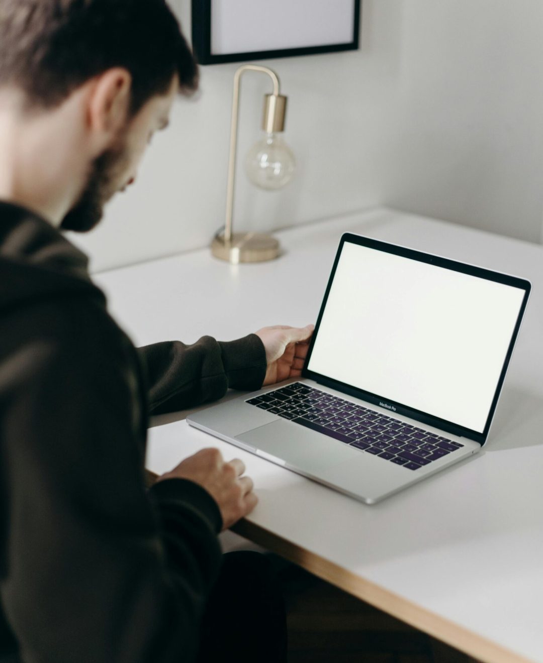 Adult man in hoodie using laptop at home with blank screen. Minimalist home office setting.