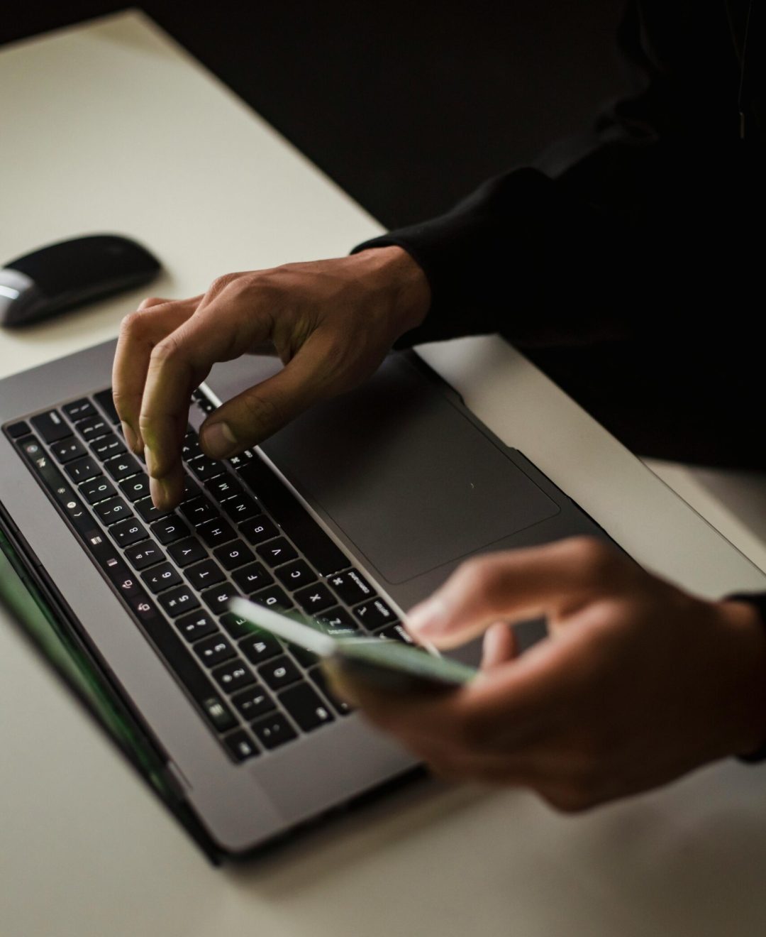High angle crop male in black clothes browsing contemporary netbook and mobile phone while working in office